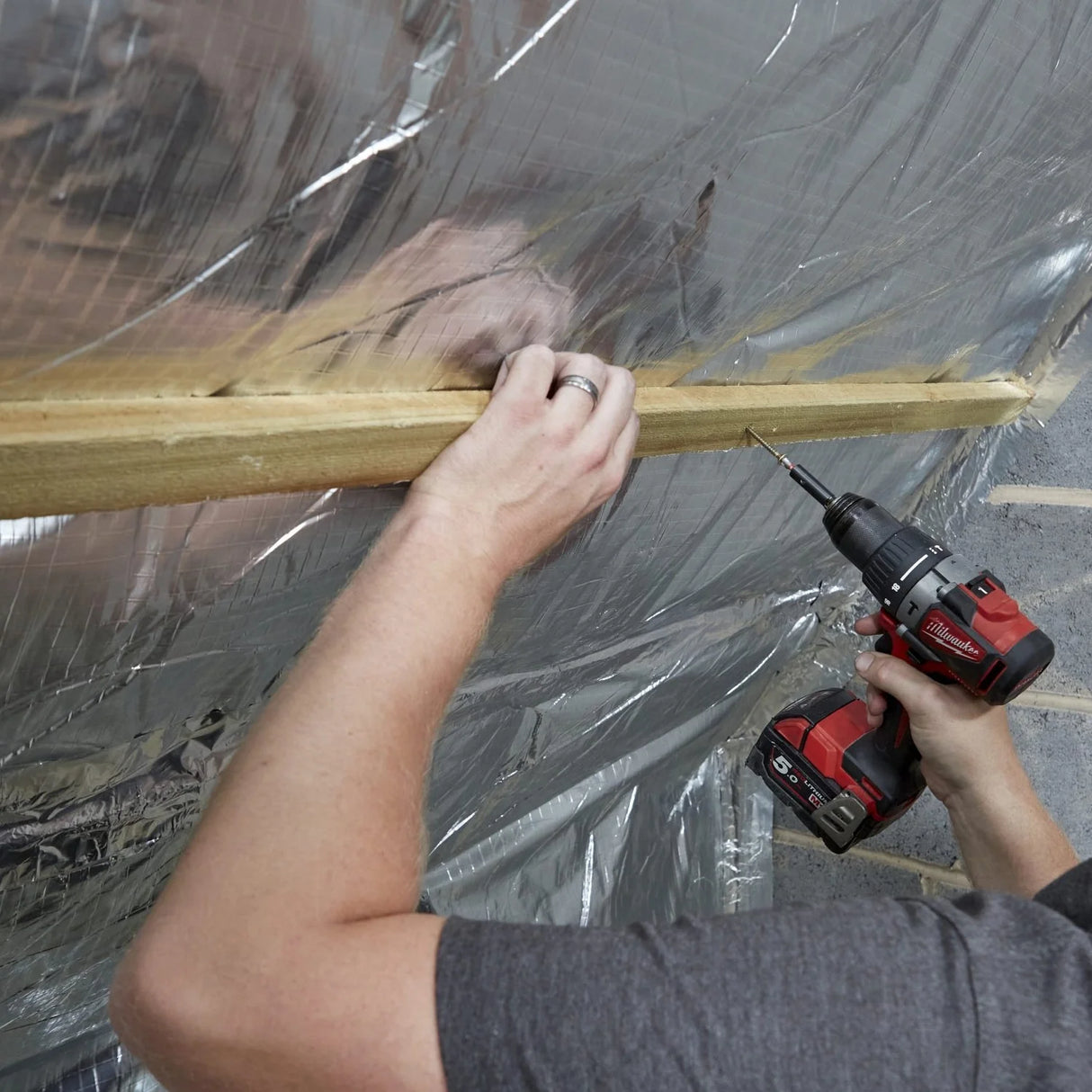 Person using a drill to secure timber battens over multi-foil insulation