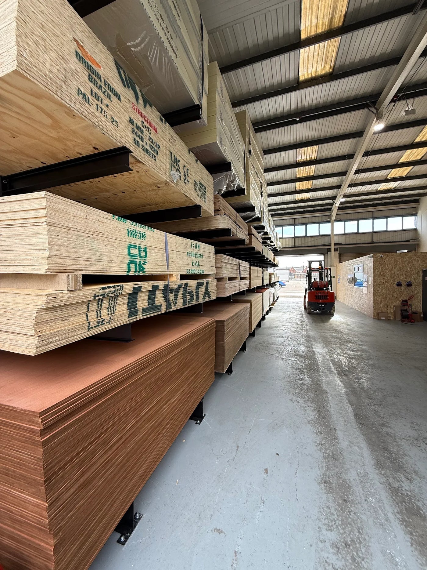 Stacks of sheet materials in a warehouse with a forklift in the background