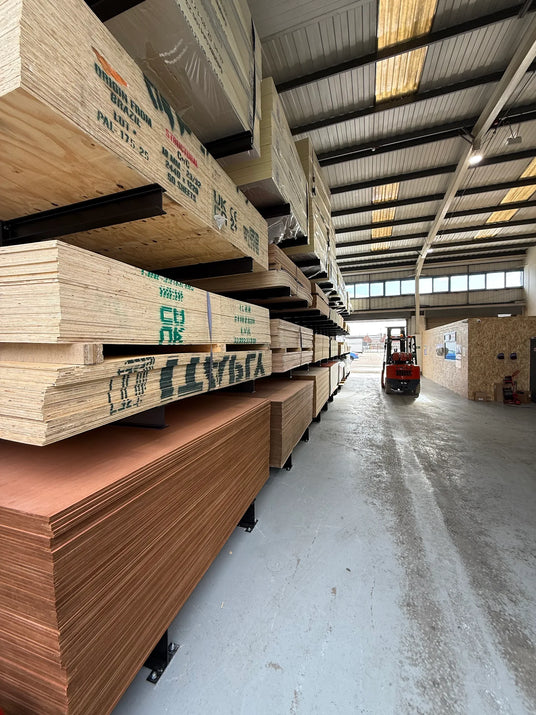 Stacks of sheet materials in a warehouse with a forklift in the background